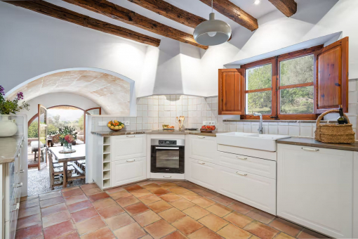 Cocina luminosa de estilo rústico con vigas de madera, suelo de terracota y acceso a la terraza